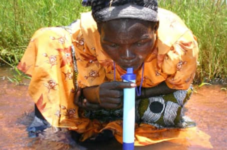A woman is holding a blue bottle and drinking water.