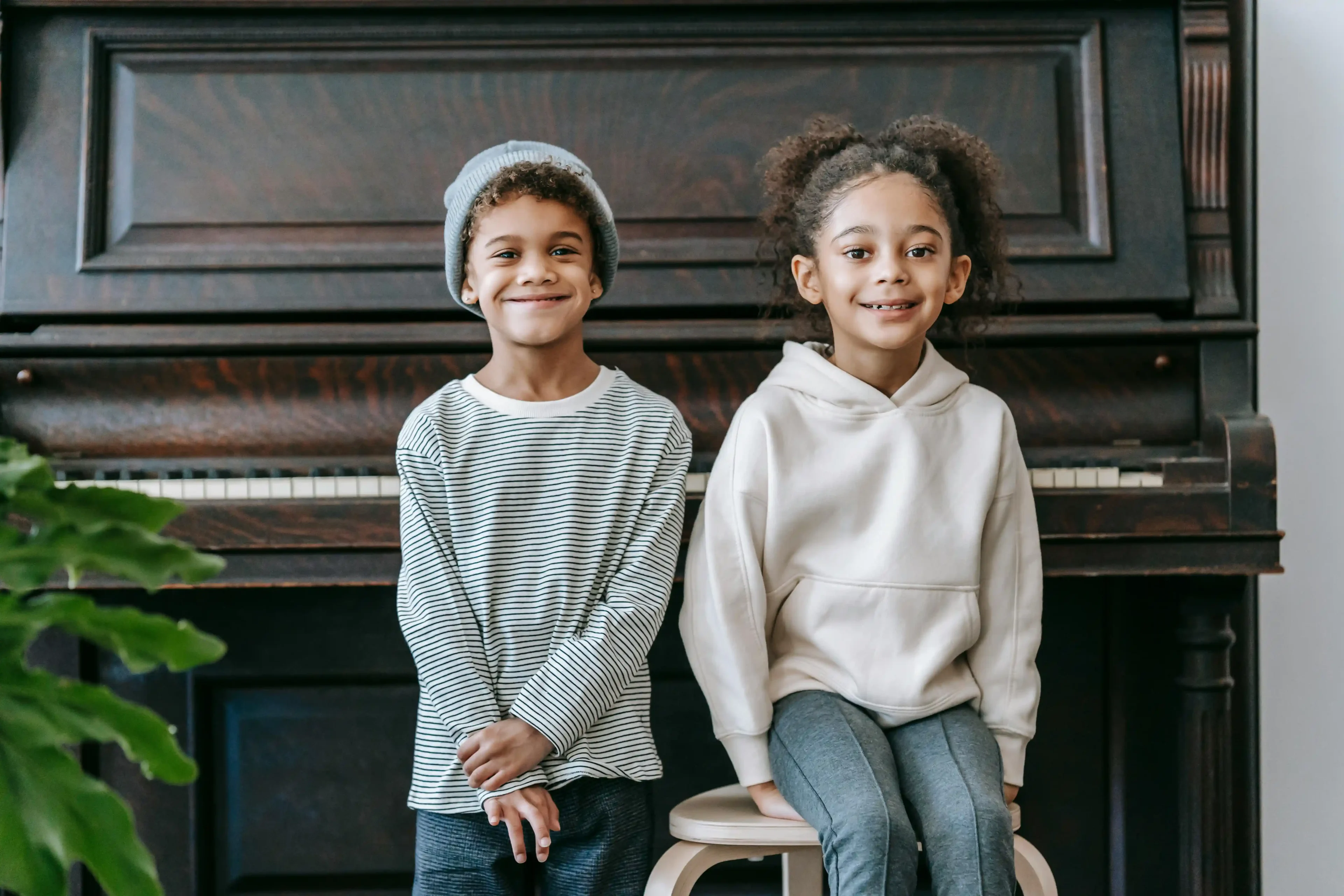 Two children sitting on a stool in front of a piano.