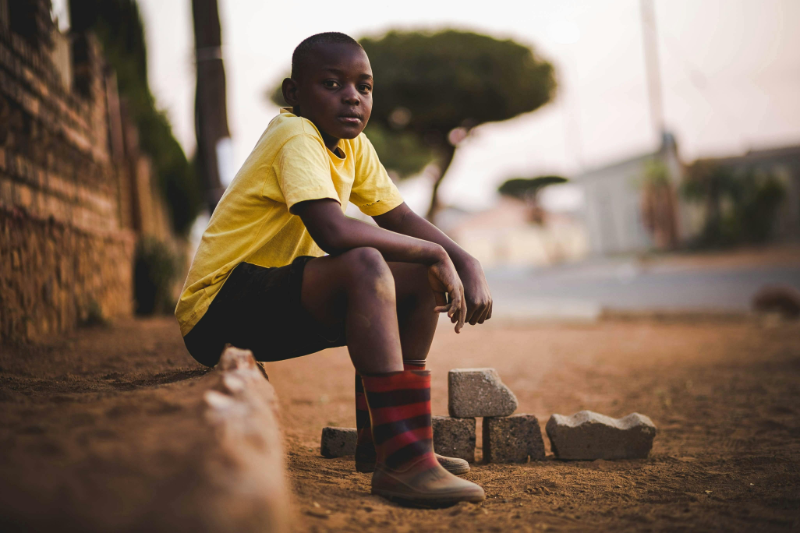 A young boy sitting on the ground in his boots.