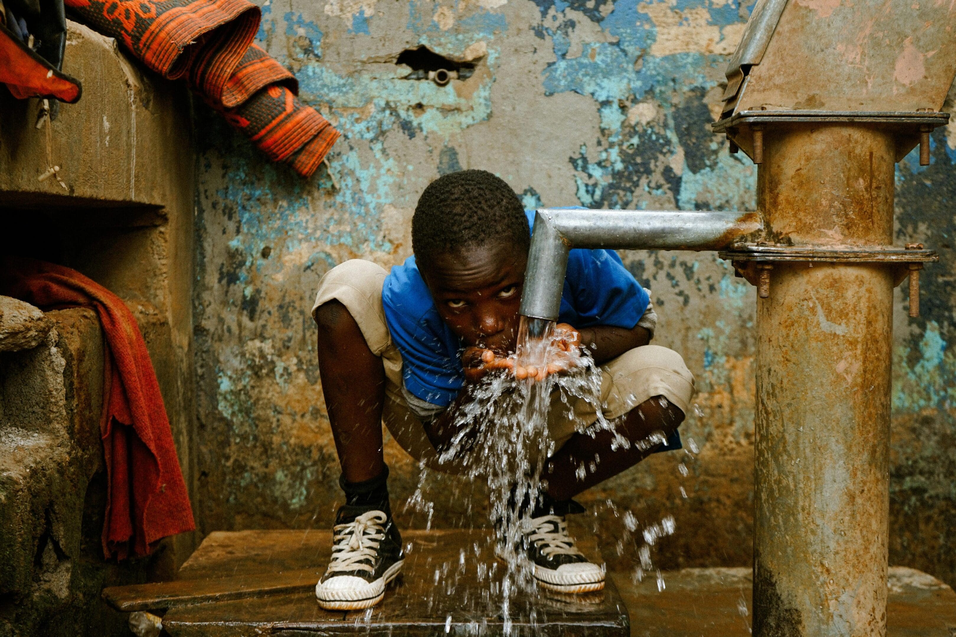 A boy is drinking water from the pipe.