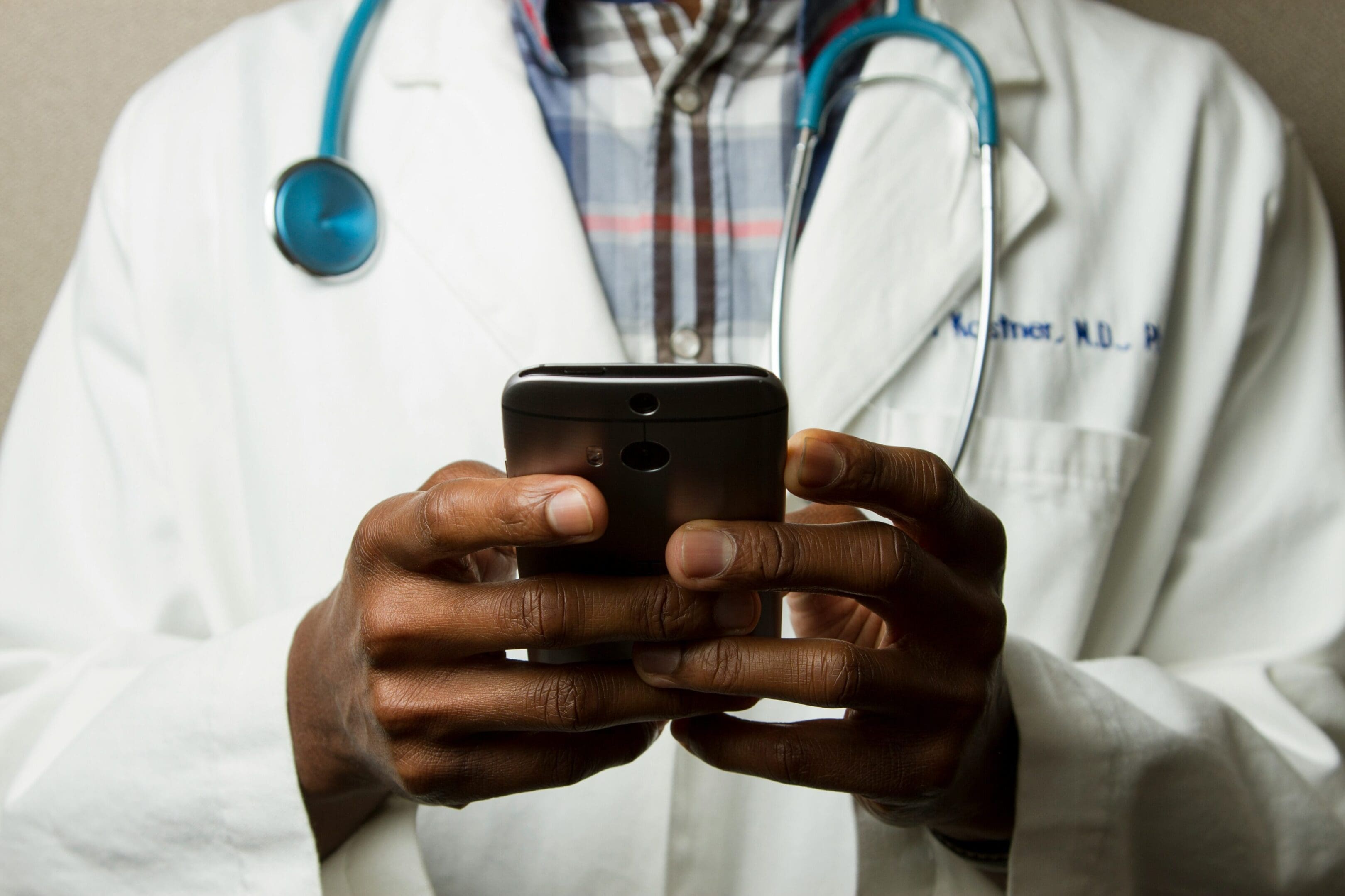 A doctor is holding his phone while wearing a stethoscope.